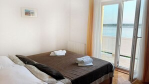 Ein Schlafzimmer mit Bett, einem Fenster mit Vorhängen und Blick aufs Meer.