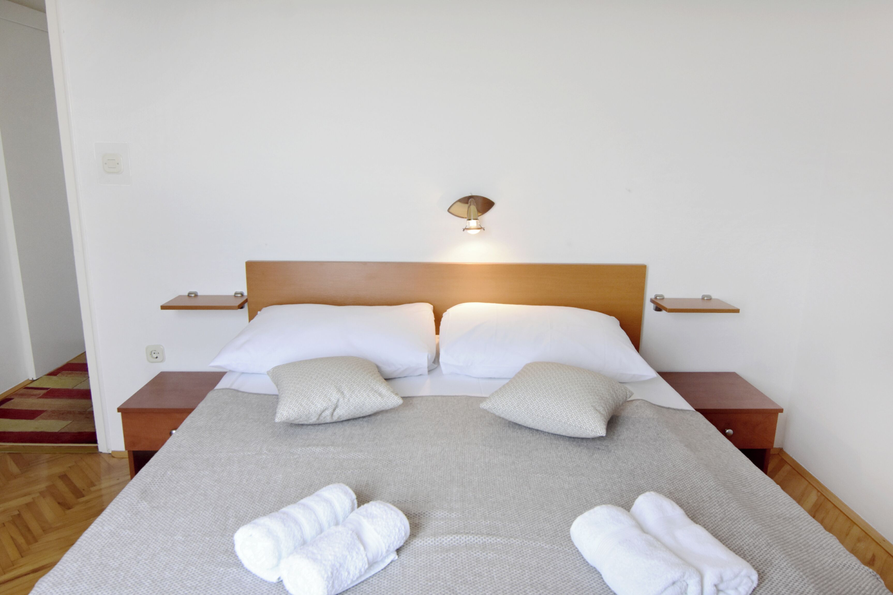 A neatly made bed with pillows, a bedside table, a wall-mounted lamp, and a small shelf.