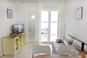 A living room with a sofa, a TV, a dining table, and a view of the sea through a glass door. - Seafront apartment on the Island of Rab (Rab)