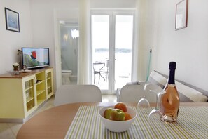 A room with a dining table, a bowl of fruit, a bottle, and a television. - Seafront apartment on the Island of Rab (Rab)