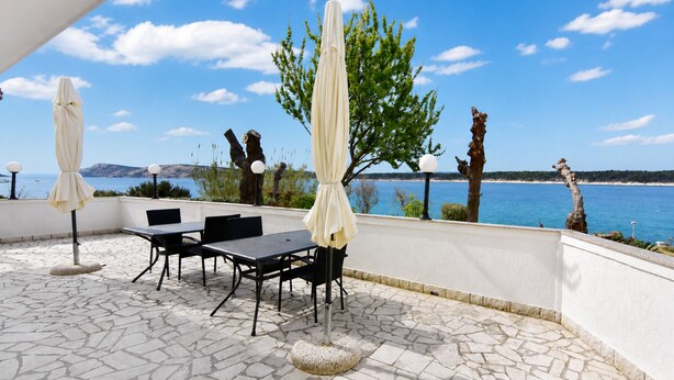 An outdoor patio with a table and chairs, a covered umbrella, and a view of the sea. - Cozy seafront flat on the Island of Rab (Rab)