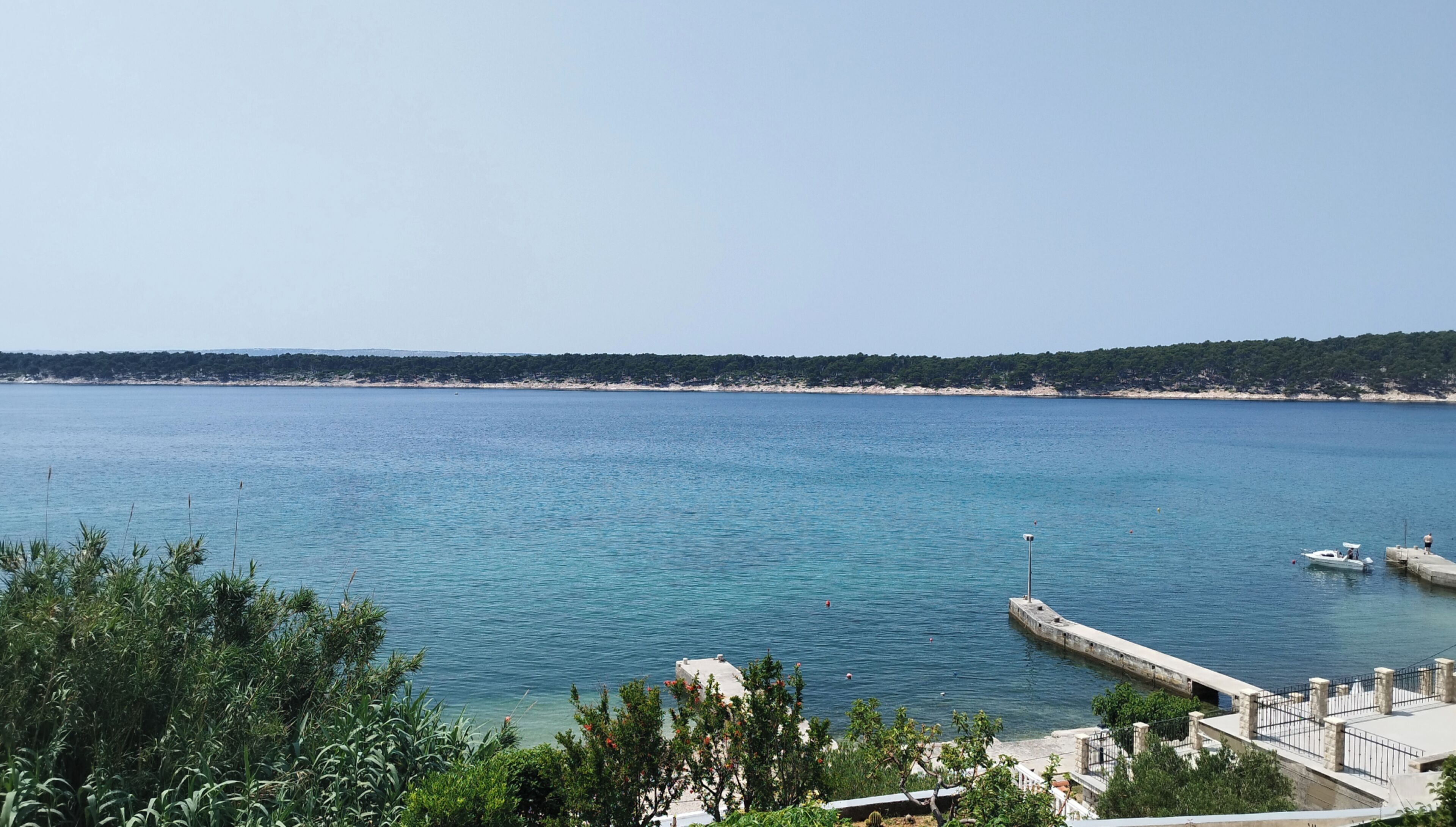 Vista costera con cielo despejado, mar tranquilo y una costa distante cubierta de árboles.