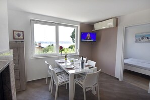 A dining area with a table set for two, a television mounted on the wall, and a bed in the adjacent room. - Cozy house in Crveni Vrh near the sea (Crveni Vrh)