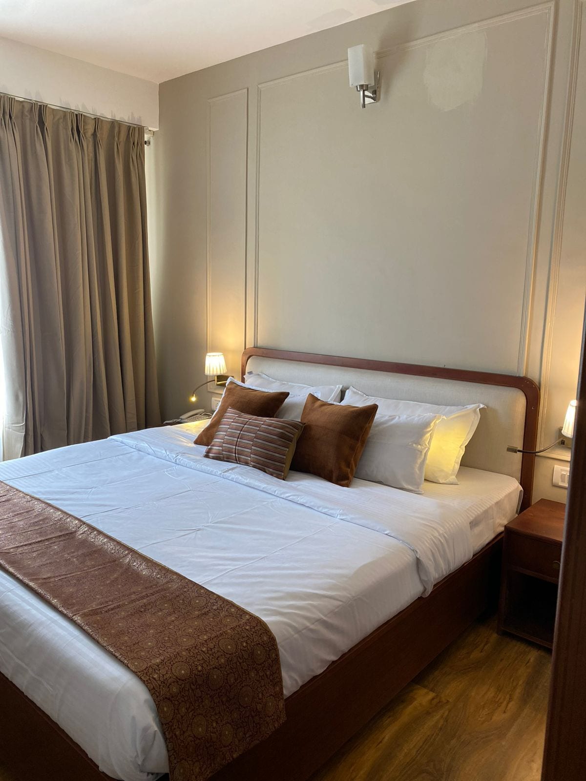 A neatly made bed with a patterned throw, bedside lamps, and a wooden nightstand.