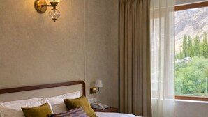 Une chambre à coucher avec un lit, des oreillers, une table de chevet, une lampe et une fenêtre avec des rideaux.