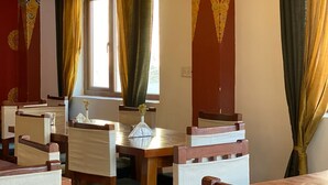Un espace repas avec des tables et des chaises en bois, une fenêtre avec des rideaux et des motifs décoratifs sur les murs.