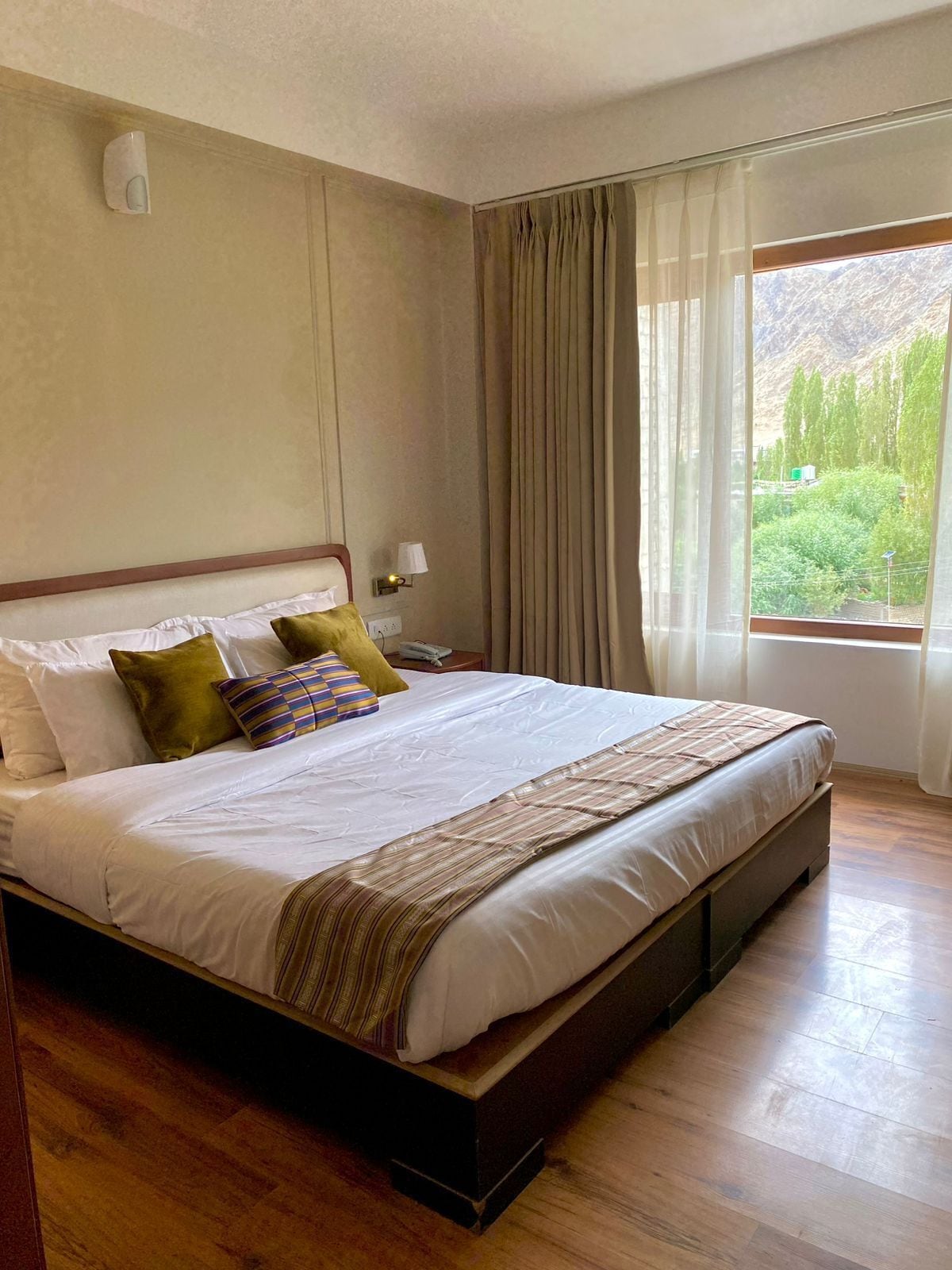 A hotel room with a large bed, a nightstand, a lamp, and a window with curtains.