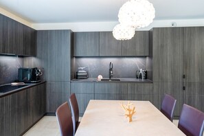 Een moderne keuken met donkerhouten kasten, een centraal eiland en een eethoek met tafel en stoelen.