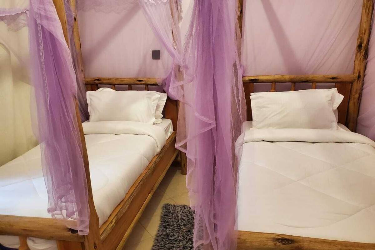 Two wooden beds with white linens and purple canopy drapes.