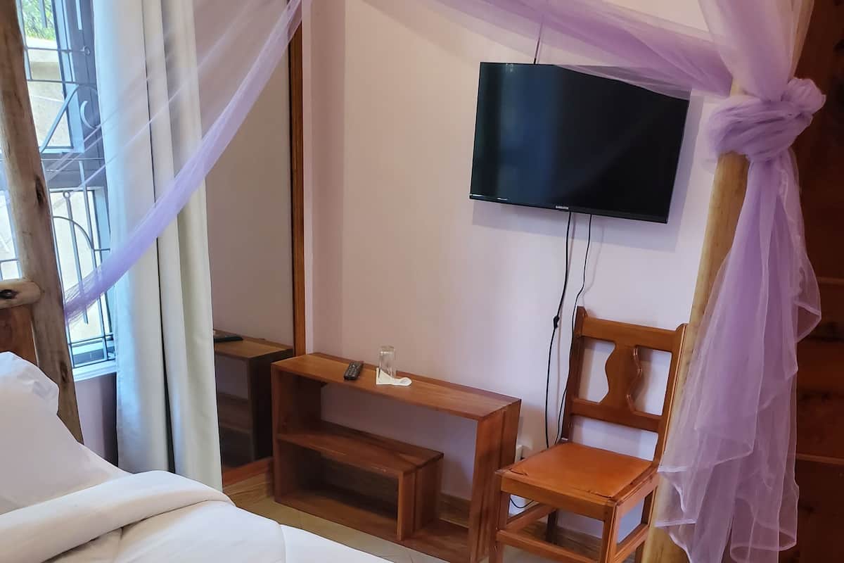 A room with a bed, a wooden chair, a small table, and a TV mounted on the wall.