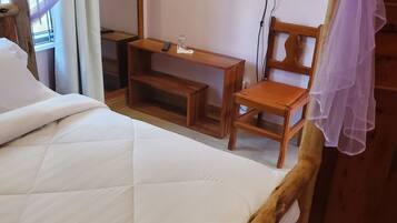 Een kamer met een bed, een houten stoel, een kleine tafel en een aan de muur bevestigde televisie.