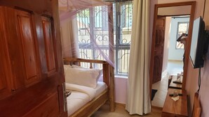 A room with a wooden bed, a small table, a TV, and a window with metal bars.