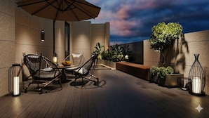 A rooftop terrace with a table, chairs, an umbrella, and potted plants. - Phoenix Crowne Vinh Hotel (Thanh Vinh)