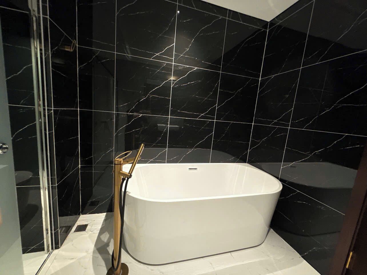 Une salle de bain moderne avec une baignoire sur pieds, une douche à parois de verre et des murs en marbre noir.