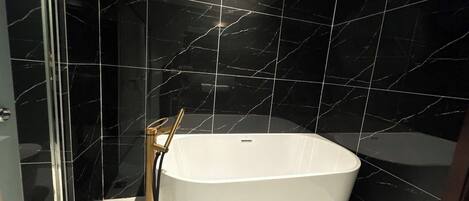 Une salle de bain moderne avec une baignoire sur pieds, une douche à parois de verre et des murs en marbre noir.