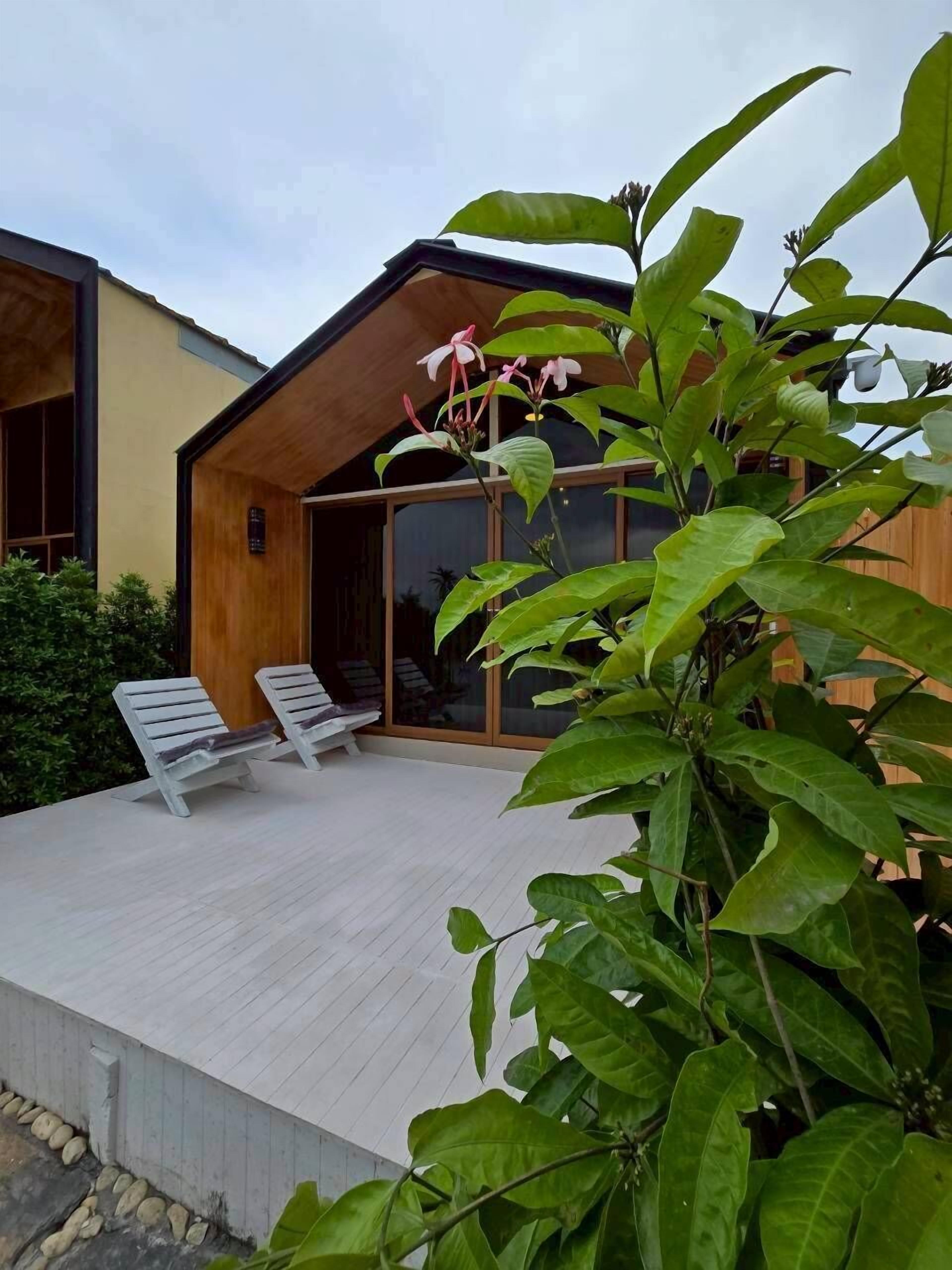 Uma casa moderna com um deck de madeira, duas poltronas de descanso e uma grande janela.