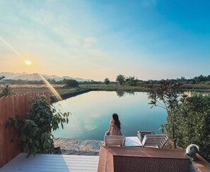 A serene outdoor setting with a wooden deck, lounge chairs, and a view of a calm lake with mountains in the background. - Kiangnapa Cottage (Kanchanaburi)