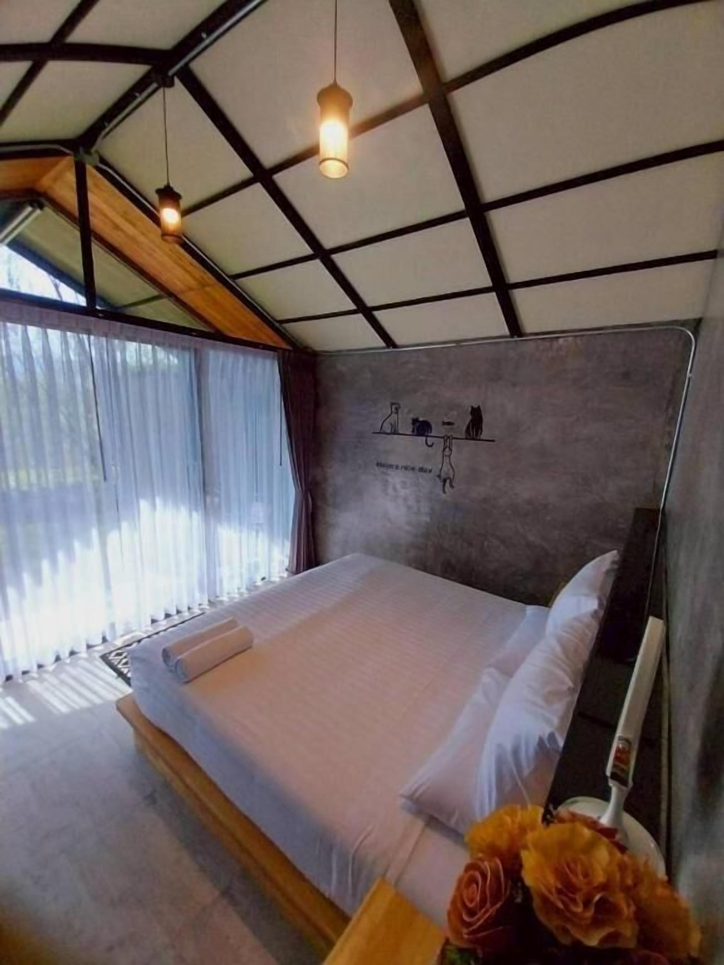 Een slaapkamer met een bed, een nachtkastje, een vaas met bloemen en een muur met een illustratie van een kat.