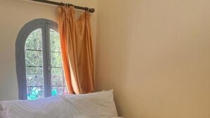 A bedroom with a bed, a window with curtains, and a floral bedspread. - Hôtel Restaurant ASGAOUR (Asgaour)