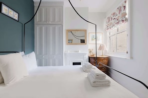 A bedroom with a bed, a dresser, a mirror, and a window with curtains. - Refined 2BD Home in Fulham (London)