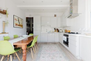 A modern kitchen with white cabinetry, a wooden dining table, and green chairs. - Refined 2BD Home in Fulham (London)