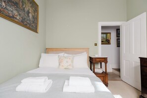 A neatly made bed with white linens and folded towels, a wooden bedside table with a book, and a painting on the wall. - Refined 2BD Home in Fulham (London)