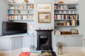 A living room with a fireplace, bookshelves, a television, and magazines. - Refined 2BD Home in Fulham (London)