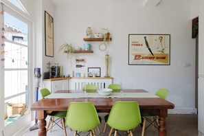 Un coin repas avec une table en bois, des chaises vertes et une affiche accrochée au mur.