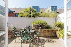A patio with a table and chairs, surrounded by potted plants and a brick wall. - Refined 2BD Home in Fulham (London)