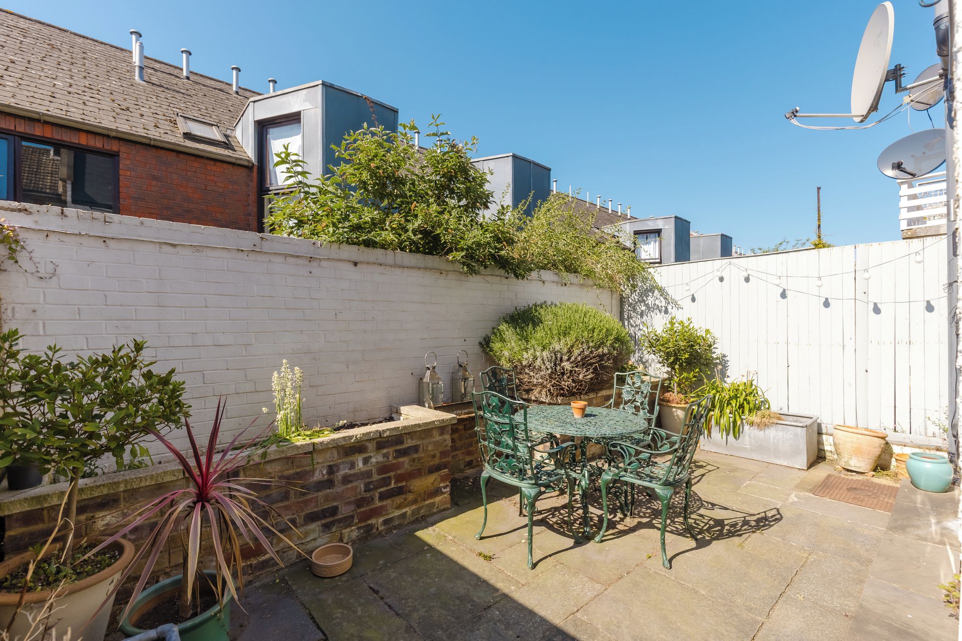 A rooftop garden with potted plants, a metal table, and chairs.