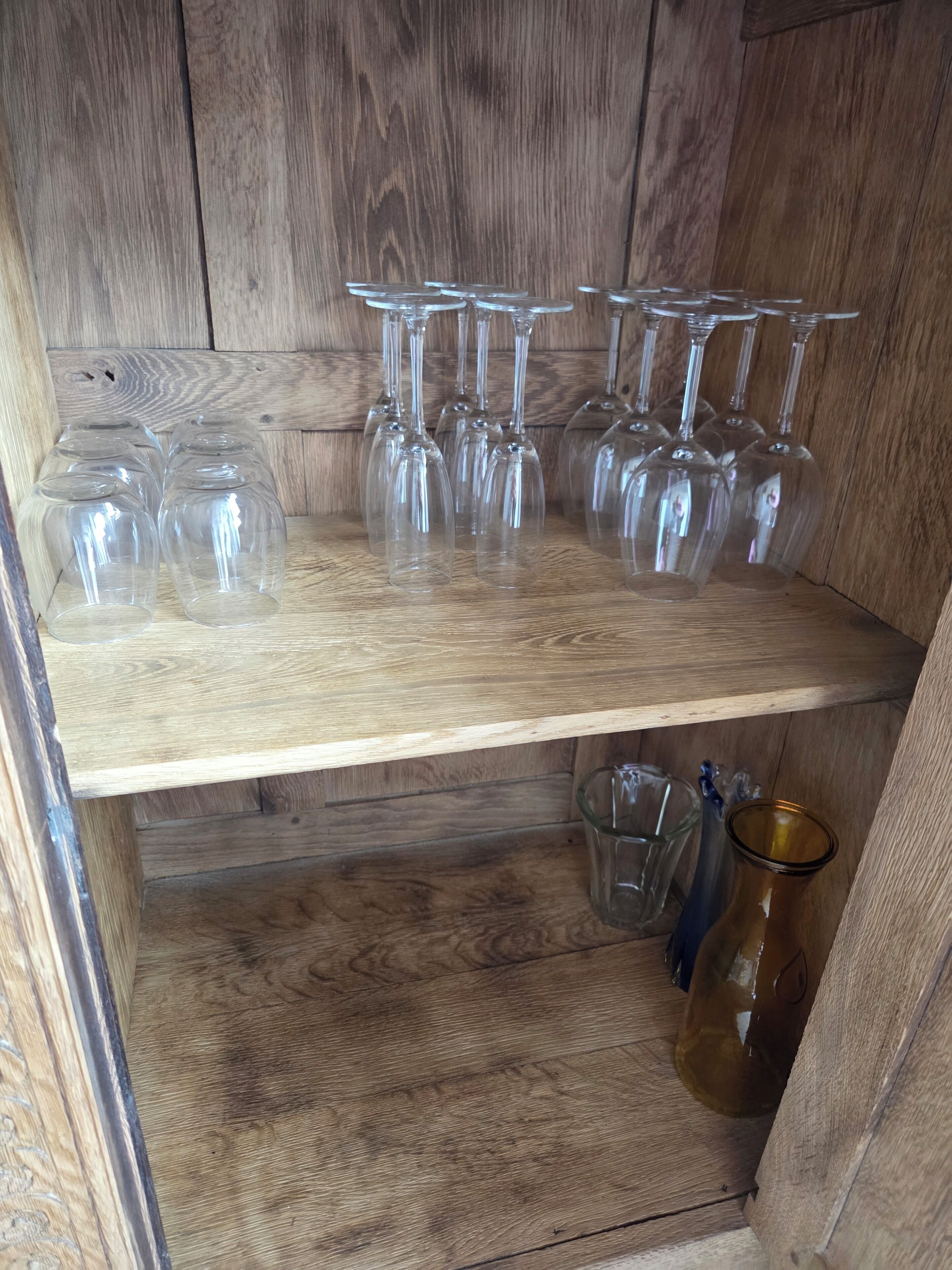 Una estantería de madera con varios vasos de vino y una jarra de vidrio.