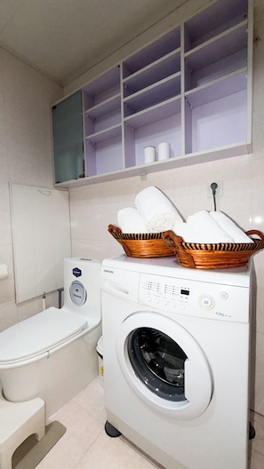 Ein Waschraum mit Waschmaschine, Toilette und Ablage für Handtücher.