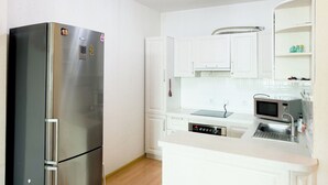 Una cucina moderna con mobili bianchi, un frigorifero in acciaio inossidabile, un forno a microonde e uno sgabello da bar.