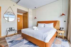 A hotel room with a bed, a bedside table with a phone, a mirror on the wall, and a chair. - Free housekeeping visits during your stay - StayShort - Stylish Studio in JVT Sleeps 2 with Balcony (JVT)