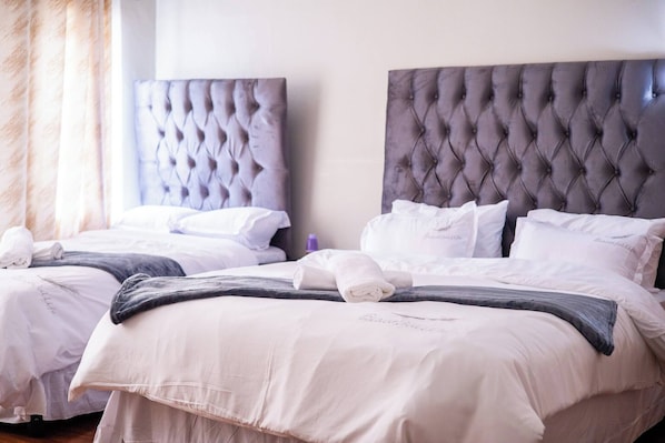 A hotel room with two beds, each with a tufted headboard, white bedding, and a neatly folded towel. - Luxurious Mansion Whole (Johannesburg)