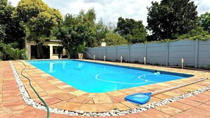 Una piscina rectangular con solárium empedrado, rodeada por un muro de piedra bajo y una cerca alta.
