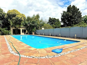 A rectangular swimming pool with a tiled deck, surrounded by a low stone wall and a tall fence. - Luxurious Mansion Whole (Johannesburg)