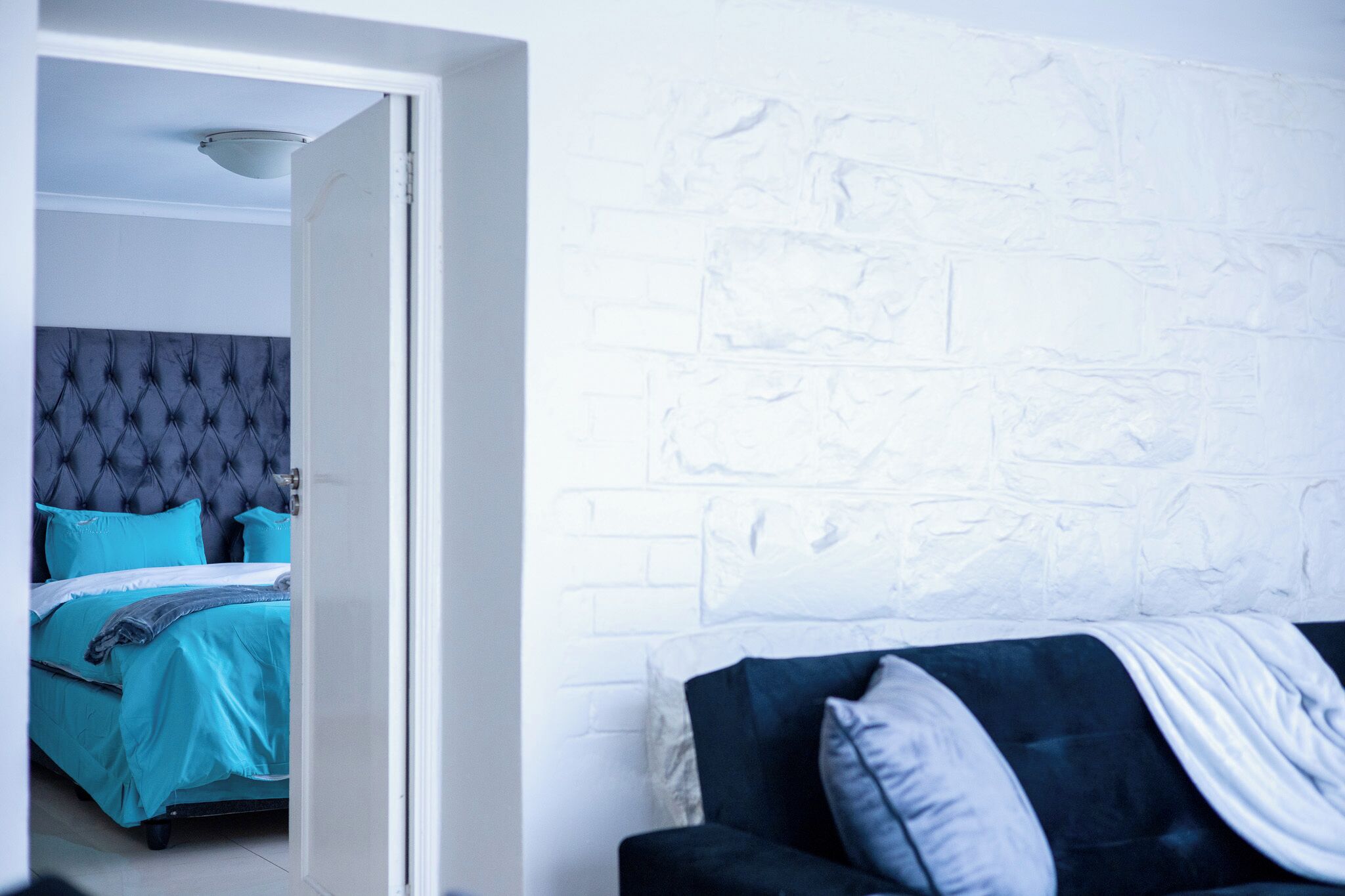 Een kamer met een bed, een donkergrijze bank en een witte bakstenen muur.