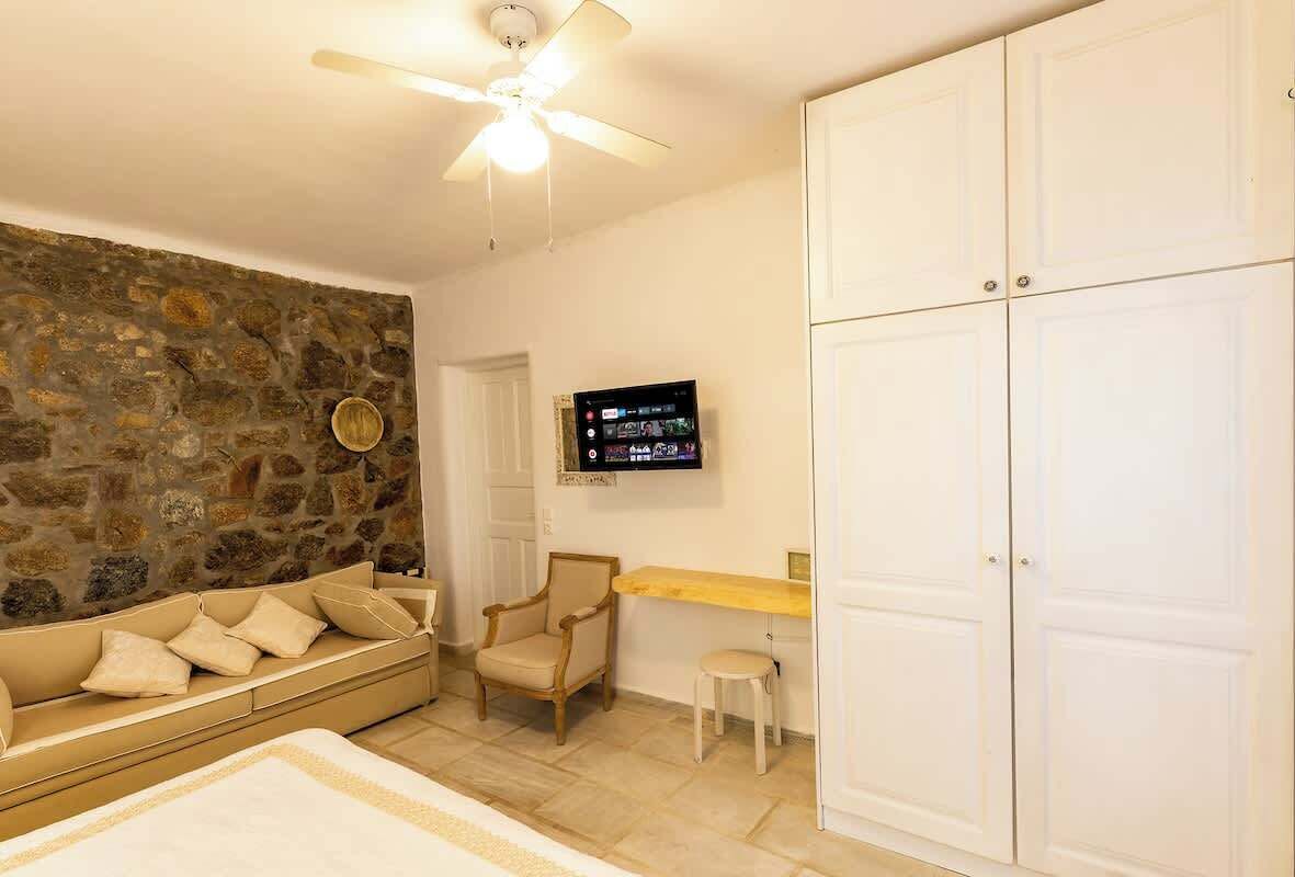 Una stanza con parete in pietra, un divano, una poltrona, una TV e un armadio.