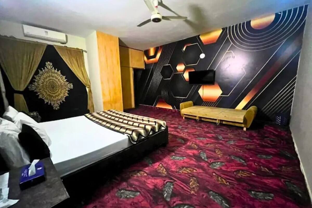 Un dormitorio con cama, sofá, ventilador de techo y una pared con patrones geométricos.
