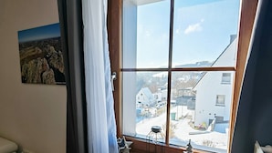 A room with a large window, a small table with a lantern, a star-shaped decoration, and a painting on the wall.