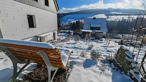 A snow-covered bench outside a building with a view of a snowy landscape and distant hills.