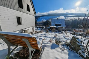 En snötäckt bänk utanför en byggnad med utsikt över ett snöigt landskap och avlägsna kullar.