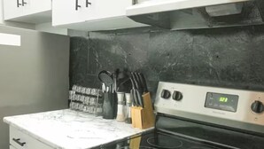 A kitchen with a black stove, white cabinets, and a marble countertop. - Main Downtown-Deluxe Suite w Pool, Gym & Balcony (Winnipeg)