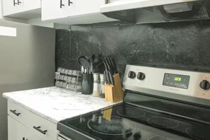 Een keuken met een zwart fornuis, witte kasten en een marmeren aanrecht.