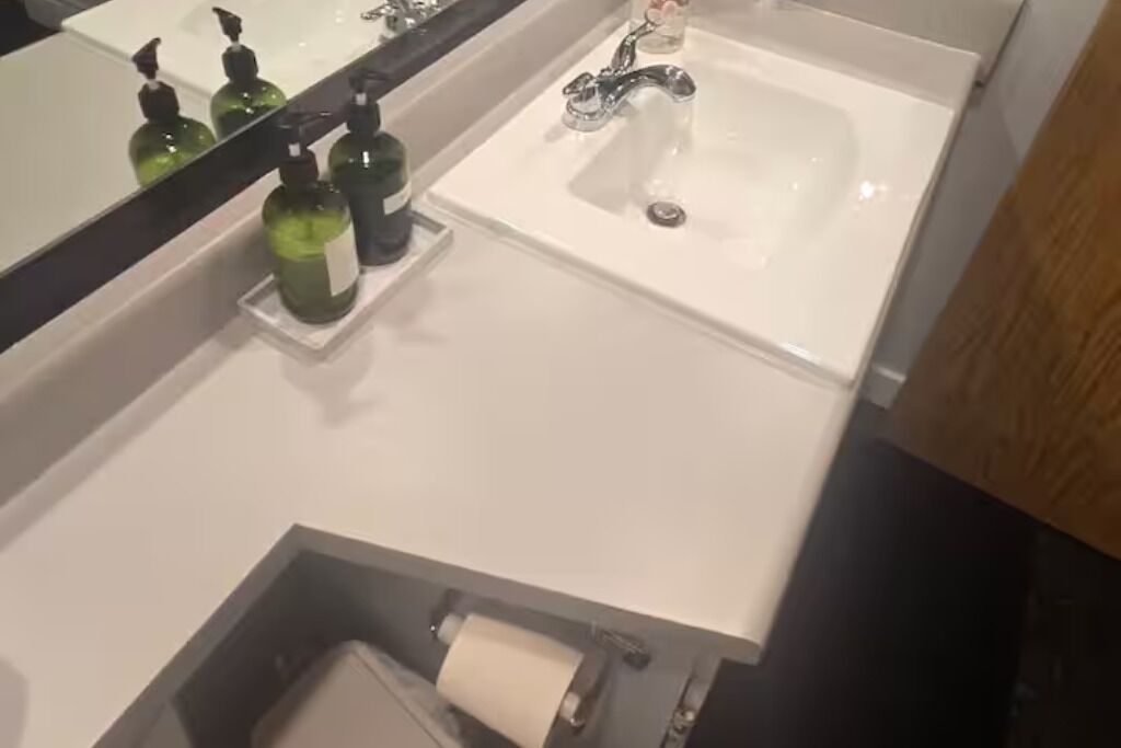 Un baño con un lavamanos blanco, un espejo y dos botellas verdes sobre la encimera.