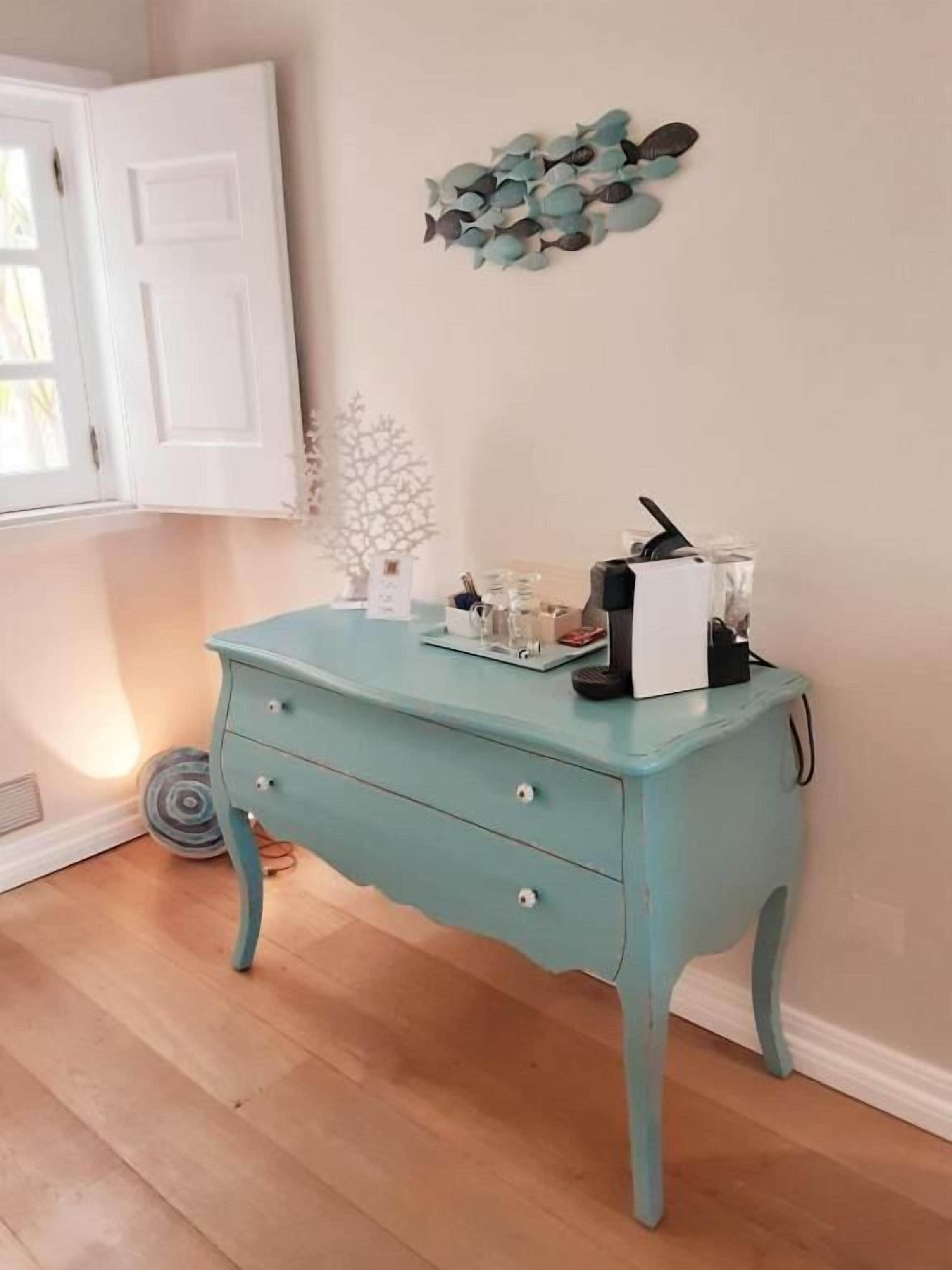 A teal-colored dresser with drawers, a white door, and a wall-mounted decorative piece.