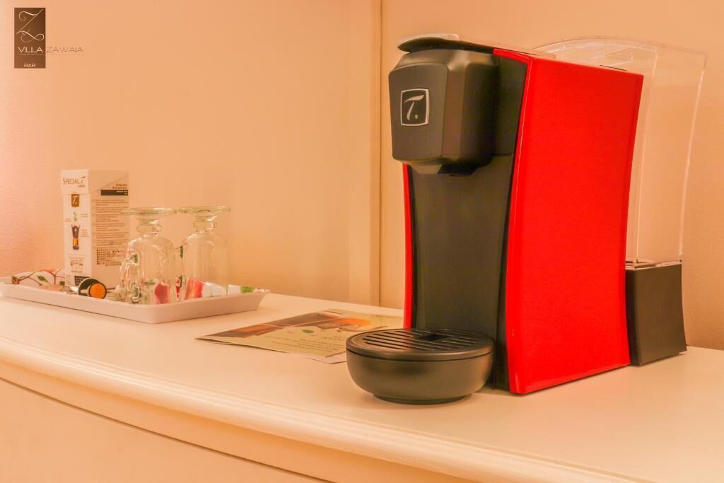 A coffee machine with a red and black design, a glass carafe, and a small black cup on a white counter.