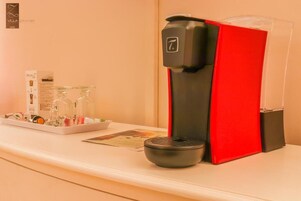 A coffee machine with a red and black design, a glass carafe, and a small black cup on a white counter.