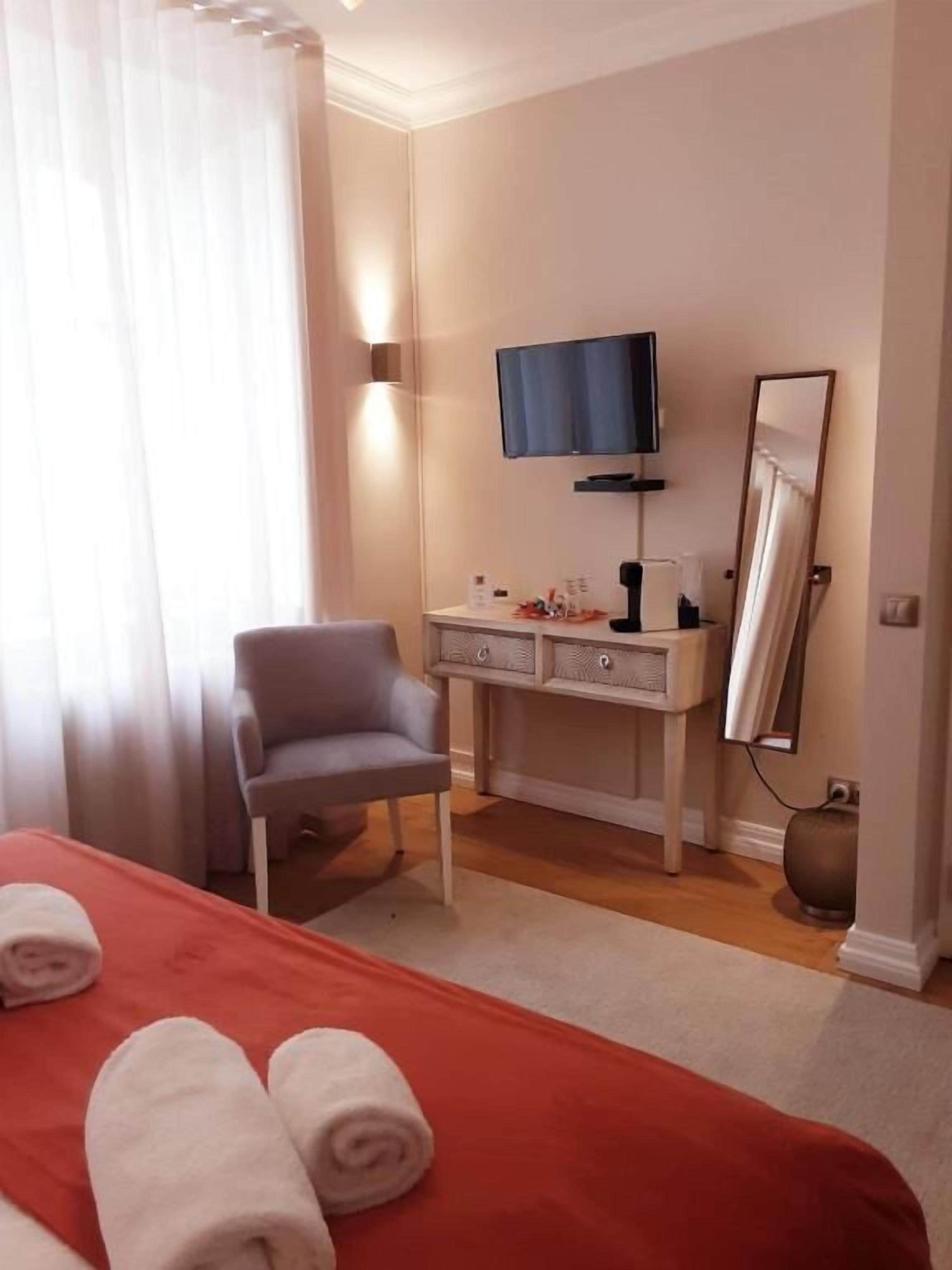 A hotel room with a bed, a chair, a TV, a mirror, and a desk with drawers.